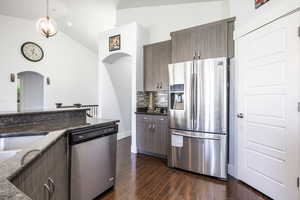 Kitchen featuring stainless steel appliances, arched walkways, decorative backsplash, dark wood-type flooring, and dark stone counters