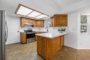 Kitchen featuring appliances with stainless steel finishes, under cabinet range hood, a sink, a peninsula, and upgraded quartz countertop.