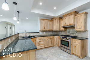 Kitchen with under cabinet range hood, stainless steel gas range oven, light brown cabinetry, and a sink
