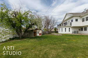 View of yard featuring central AC unit, fence, an outdoor structure, and a balcony