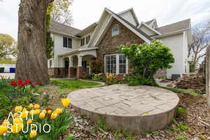 View of front of property with central air condition unit, roof with shingles, a patio area, and stone siding