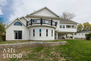 Rear view of house with fence, a balcony, stucco siding, a ceiling fan, and a lawn