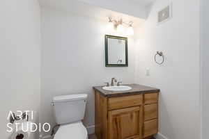 Half bath with vanity, toilet, baseboards, and visible vents