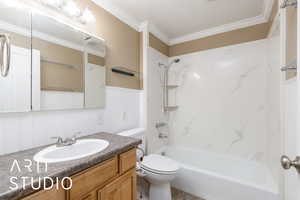 Full bathroom featuring toilet, ornamental molding, vanity, bathtub / shower combination, and a wainscoted wall