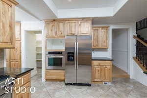 Kitchen featuring light brown cabinets, dark stone countertops, appliances with stainless steel finishes, and visible vents