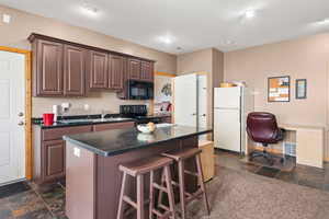 Kitchen featuring black appliances, stone tile flooring, dark countertops, a kitchen breakfast bar, and a kitchen island