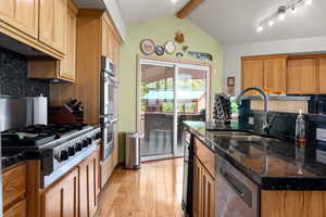 Kitchen featuring appliances with stainless steel finishes, hickory hardwood finished floors, tasteful backsplash, and dark stone countertops