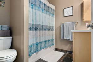 Full bath with baseboards, stone tile flooring, vanity, and shower / tub combo