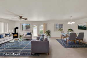 Carpeted living area featuring a wood stove, a chandelier, and a ceiling fan