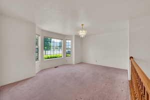 Unfurnished room featuring a chandelier, light carpet, and baseboards