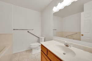 Bathroom featuring tile patterned flooring, vanity, toilet, a bath, and baseboards