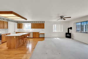 Kitchen featuring appliances with stainless steel finishes, a wood stove, a ceiling fan, a breakfast bar, and light countertops