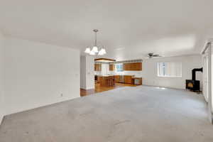 Unfurnished living room featuring a wood stove, ceiling fan, a chandelier, light carpet, and baseboards