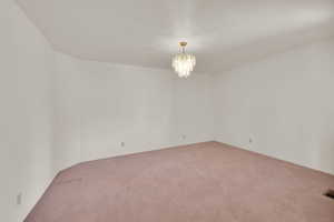 Unfurnished room featuring light colored carpet, a chandelier, and baseboards