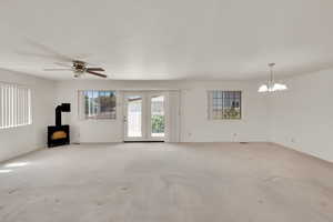 Unfurnished living room with a wood stove, carpet, a chandelier, ceiling fan, and baseboards