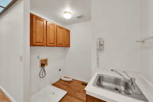 Laundry area with electric dryer hookup, cabinet space, washer hookup, and light wood-style flooring