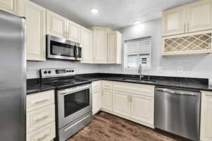 Kitchen featuring stainless steel appliances, a sink, dark wood-style floors, cream cabinets, and recessed lighting