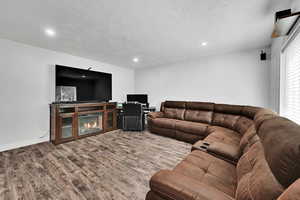 Living area with wood finished floors, recessed lighting, a textured ceiling, a glass covered fireplace, and baseboards