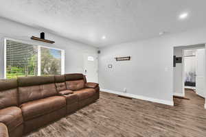 Living area featuring wood finished floors, a textured ceiling, recessed lighting, and baseboards