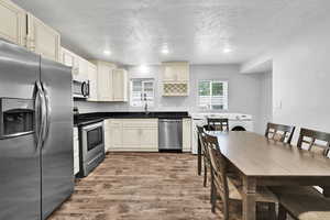 Kitchen with appliances with stainless steel finishes, a sink, dark wood finished floors, a textured ceiling, and dark countertops