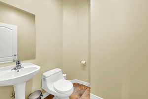 Bathroom featuring a sink, toilet, baseboards, and stone tile flooring