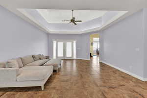 Living area featuring french doors, arched walkways, a ceiling fan, a tray ceiling, and baseboards