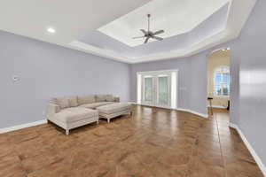 Living room featuring tile patterned floors, arched walkways, a ceiling fan, a tray ceiling, and baseboards