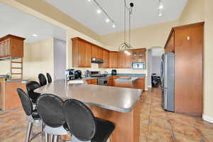 Kitchen with a peninsula, a kitchen bar, a sink, stainless steel appliances, and under cabinet range hood