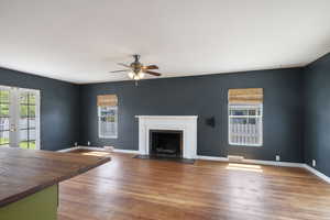 Unfurnished living room with a ceiling fan, a fireplace with flush hearth, wood finished floors, baseboards, and french doors