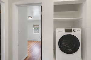 Clothes washing area with washer / dryer, wood finished floors, and baseboards