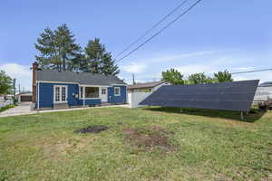 Back of house with entry steps, solar panels, a chimney, and roof with shingles