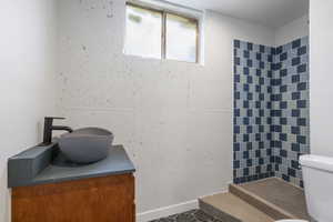 Bathroom featuring toilet, a tile shower, and vanity