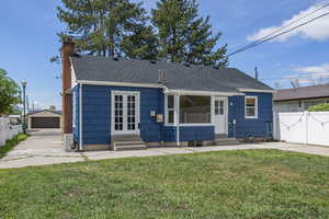 Bungalow with entry steps, a chimney, a shingled roof, a detached garage, and an outbuilding