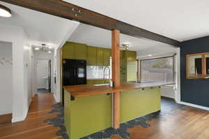 Kitchen featuring butcher block counters, a sink, green cabinetry, freestanding refrigerator, and dark wood-style floors