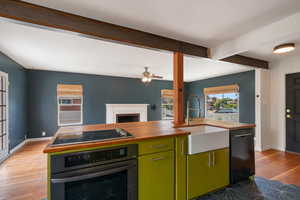 Kitchen featuring black appliances, butcher block counters, a sink, green cabinets, and light wood-style floors