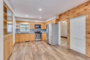 Kitchen with stainless steel appliances, a sink, tasteful backsplash, light brown cabinets, and LVP flooring