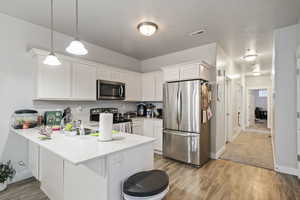 Kitchen with appliances with stainless steel finishes, a peninsula, white cabinets, light wood finished floors, and light countertops