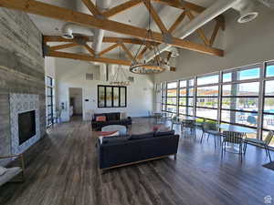 Living area with high vaulted ceiling, healthy amount of natural light, beam ceiling, a chandelier, and wood finished floors