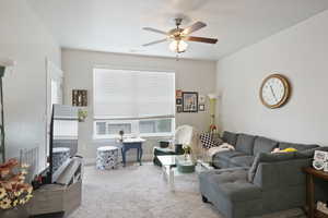 Carpeted living area featuring a ceiling fan and baseboards