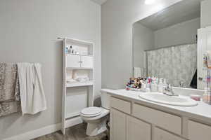 Bathroom with toilet, wood finished floors, vanity, a shower with curtain, and baseboards