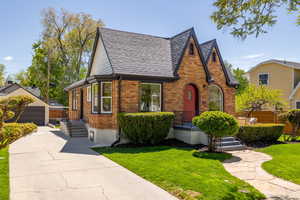 English style home with an outbuilding, brick siding, roof with shingles, a front yard, and a detached garage
