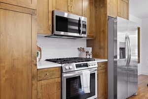 Kitchen featuring stainless steel appliances, tasteful backsplash, light countertops, and light wood finished floors