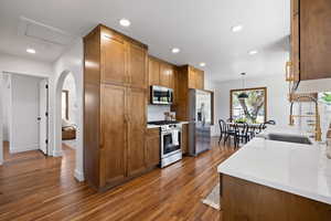 Kitchen with appliances with stainless steel finishes, a sink, baseboards, dark wood-type flooring, and brown cabinetry