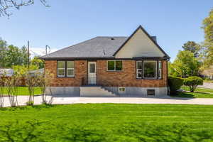 Rear view of house featuring a lawn, brick siding, and a shingled roof