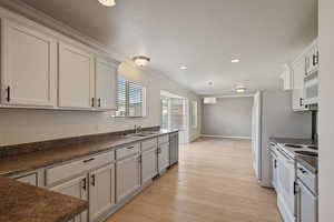 Kitchen with white appliances, a sink, dark countertops, light wood-style floors, and crown molding