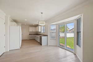 Kitchen with freestanding refrigerator, ornamental molding, dishwasher, dark countertops, and light wood-type flooring