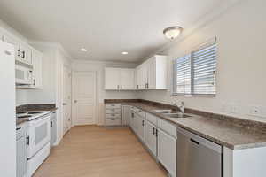 Kitchen with white appliances, a sink, light wood finished floors, ornamental molding, and dark countertops
