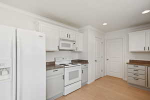 Kitchen featuring white appliances, dark countertops, light wood-style floors, crown molding, and recessed lighting