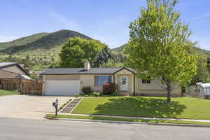 Ranch-style house featuring a mountain view, concrete driveway, a garage, a chimney, and brick siding