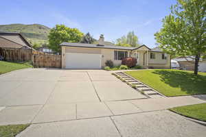 Single story home with a garage, concrete driveway, brick siding, a mountain view, and a chimney